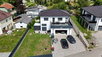 Luftaufnahme eines modernen Einfamilienhauses mit Garage, Vorgarten und gepflasterter Auffahrt.