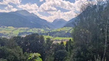 Panoramablick auf eine weite grüne Tallandschaft mit majestätischen Bergen und einem Dorf in der Ferne.