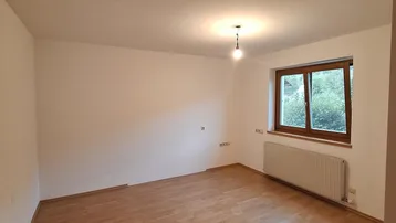 Helles Zimmer mit Holzboden, weißen Wänden und einem Fenster, das viel Tageslicht hereinlässt.