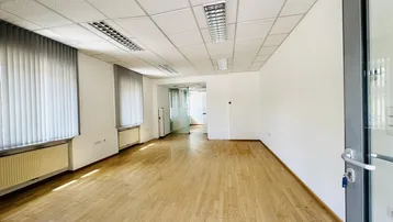 Geräumiger, heller Büroraum mit Holzfußboden, weißen Wänden und abgehängter Decke.