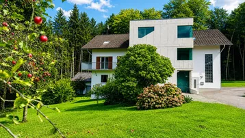 Das Anwesen präsentiert sich mit einer modernen Fassade und umgeben von üppigem Grün und Obstbäumen.