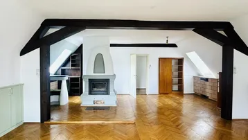 Dachzimmer mit Holzbalken, Kamin und Fischgrätparkett, das eine gemütliche Atmosphäre schafft.