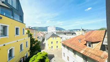 Blick über die Dächer der Stadt mit umliegenden Bergen unter blauem Himmel an einem sonnigen Tag.