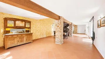Geräumiger offener Wohnbereich mit Holzbalken, Steinsäulen und Terrakottafliesen, ideal für geselliges Beisammensein.
