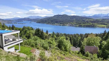 Panoramablick auf einen großen See mit umliegenden Wäldern und Bergen unter blauem Himmel.
