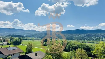 Panoramablick auf die grüne Landschaft mit Wäldern und Bergen unter blauem Himmel.