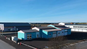 Luftaufnahme eines modernen Gewerbegebäudes mit blauer Fassade und rotem Dach unter klarem Himmel.