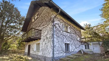 Altes Haus mit bewachsener Fassade, Balkon und Satteldach in ländlicher Umgebung.