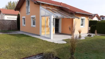 Modernes Einfamilienhaus mit orangefarbener Fassade, Wintergarten und gepflegtem Gartenbereich.
