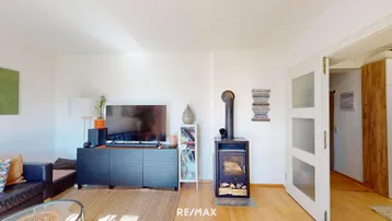 Gemütliches Wohnzimmer mit Holzboden, Fernseher und einem modernen Holzofen für warme Abende.