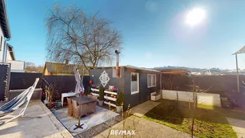 Sonniger Gartenbereich mit kleiner Hütte, Terrasse, Hängematte und Rasenfläche für Entspannung im Freien.