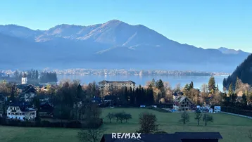 Panoramablick auf den Wolfgangsee mit umliegenden Bergen und einem Dorf mit Neubauprojekt.