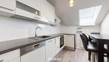 Moderne Küche mit weißen Schränken, dunkler Arbeitsplatte, Einbaugeräten und einem kleinen Essbereich.