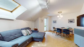 Helles Wohn- und Esszimmer mit gemütlichem Sofa, Esstisch und Dachfenster in einem Dachgeschoss.