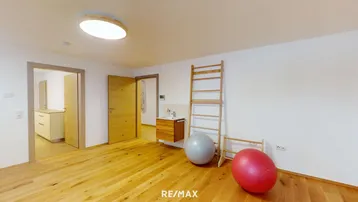 Geräumiger Mehrzweckraum mit hellem Holzboden, weißen Wänden und einem Waschbecken, der vielseitig genutzt werden kann.
