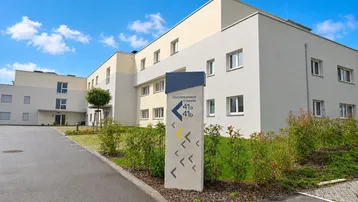Modernes Mehrfamilienhaus mit heller Fassade und Wegweiser zur Adresse.