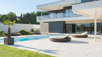 Moderne Villa mit großzügiger Terrasse, Swimmingpool und Liegeflächen unter strahlend blauem Himmel.