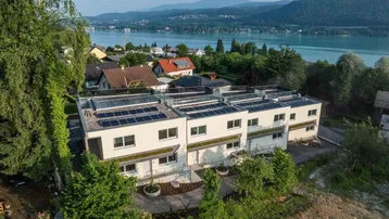 Moderne Reihenhäuser mit Seeblick und Photovoltaikanlagen auf den Dächern, umgeben von viel Grün.