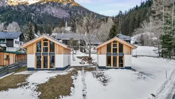 Zwei moderne Chalets in einer verschneiten Berglandschaft mit großen Fenstern und Holzelementen.