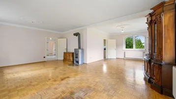 Weitläufiges Wohnzimmer mit Parkettboden, Kaminofen und Zugang zu weiteren Räumen.