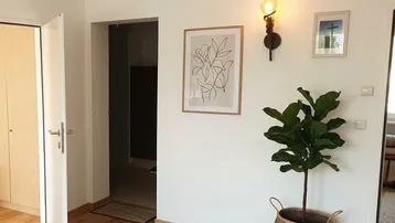 Heller Flur mit Holzboden, dekorativer Wandleuchte und Zimmerpflanze, die zu weiteren Räumen führt.