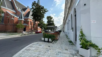 Blick auf eine belebte Straße mit einer Kirche, einem Gebäude und einer Außenterrasse mit Sitzgelegenheiten.