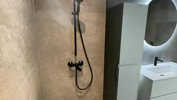 Modernes Badezimmer mit begehbarer Dusche, beleuchtetem Spiegel und eleganten grauen Fliesen.