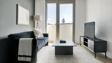 Modernes Wohnzimmer mit dunklem Sofa, Teppich und Zugang zum Balkon mit Stadtblick.
