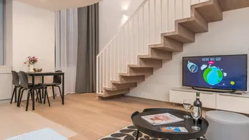 Heller Wohn- und Essbereich mit moderner Holztreppe, Parkettboden und gemütlicher Sitzecke.