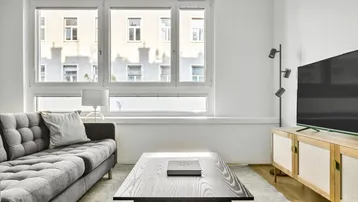 Helles Wohnzimmer mit modernem Sofa, Couchtisch und großen Fenstern mit Blick auf die Stadt.
