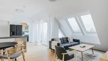 Helles Dachgeschoss-Apartment mit offenem Wohn-Essbereich, Küche und großen Dachfenstern.