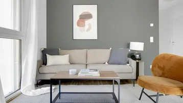 Modernes Wohnzimmer mit beigem Sofa, grauem Teppich und einem großen Fenster.