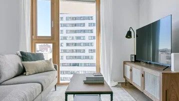 Helles Wohnzimmer mit modernem Sofa, Fernseher und Blick auf die Stadt.