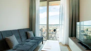 Helles Wohnzimmer mit bequemem Sofa, modernem TV-Möbel und Zugang zu einem Balkon mit Stadtblick.