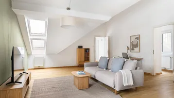 Helles Wohnzimmer im Dachgeschoss mit Holzboden, gemütlichem Sofa und Arbeitsbereich.