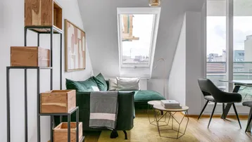 Helles Wohnzimmer mit Dachschräge, Sofa und Esstisch, sowie Zugang zum Balkon.