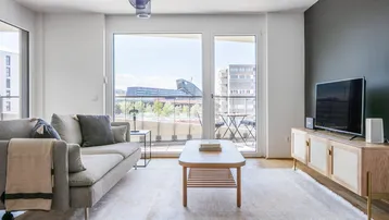 Helles Wohnzimmer mit modernem Sofa, Holzboden und Zugang zu einem Balkon mit Stadtblick.