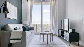 Helles Wohnzimmer mit Sofa, Fernseher und Zugang zum Balkon, modern eingerichtet.
