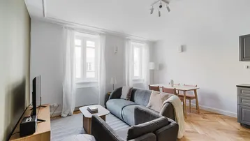 Helles Wohn- und Esszimmer mit modernem Sofa, Parkettboden und integrierter Küchenzeile.