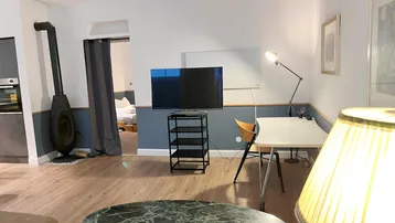 Gemütliches Wohnzimmer mit modernem Kamin, Schreibtisch und Blick in das angrenzende Schlafzimmer.