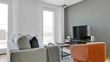 Helles Wohnzimmer mit modernem Sofa, Fernseher und Zugang zu einem Balkon.