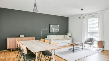 Heller offener Wohn- und Essbereich mit modernem Design, Holzboden und dunkler Akzentwand.