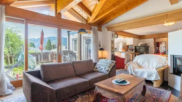 Gemütliches Wohnzimmer mit Holzbalkendecke, Kamin und Zugang zu einer sonnigen Terrasse mit Bergblick.