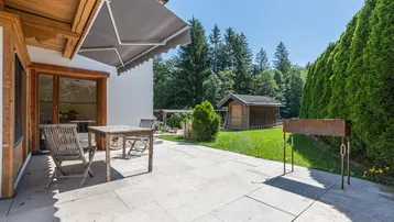Geräumige Terrasse mit Sitzgelegenheiten, Markise und Blick ins Grüne mit Gartenhaus.