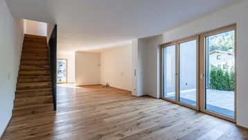 Geräumiges Wohnzimmer mit hellem Holzparkett, moderner Holztreppe und Zugang zur Terrasse.