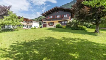 Traditionelles Haus im alpinen Stil mit großem Garten und Bergblick unter blauem Himmel.
