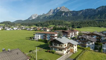 Luftaufnahme eines Hauses in ländlicher Umgebung mit beeindruckendem Bergblick und grünen Feldern.