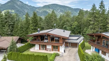 Chalet-Stil Haus mit Holzbalkonen und Bergblick, umgeben von grünen Bäumen.