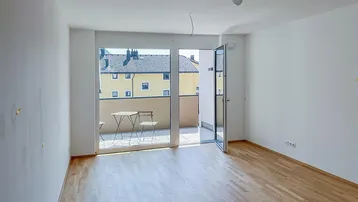 Helles Wohnzimmer mit Parkettboden und Zugang zu einem sonnigen Balkon, ideal für Entspannung.