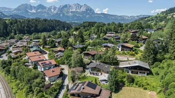 Luftaufnahme einer Wohnsiedlung in den Bergen mit vielen Häusern und grüner Landschaft.